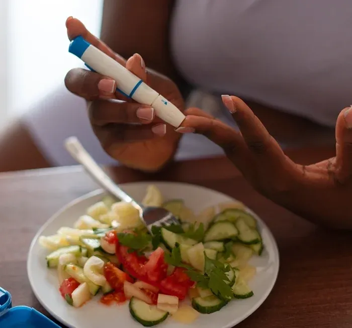 Person doing a finger-prick glucose check beside a plate of salad