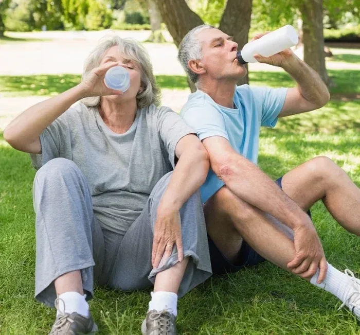 Older couple sitting on the grass drinking water after a walk